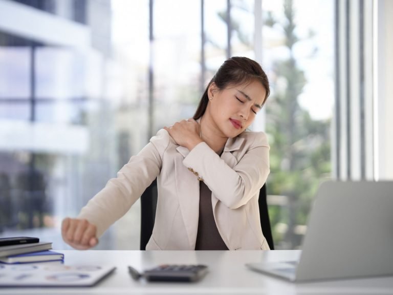 alt="A woman holding a stiff, painful shoulder, showing the loss of mobility that can be helped with functional therapy."