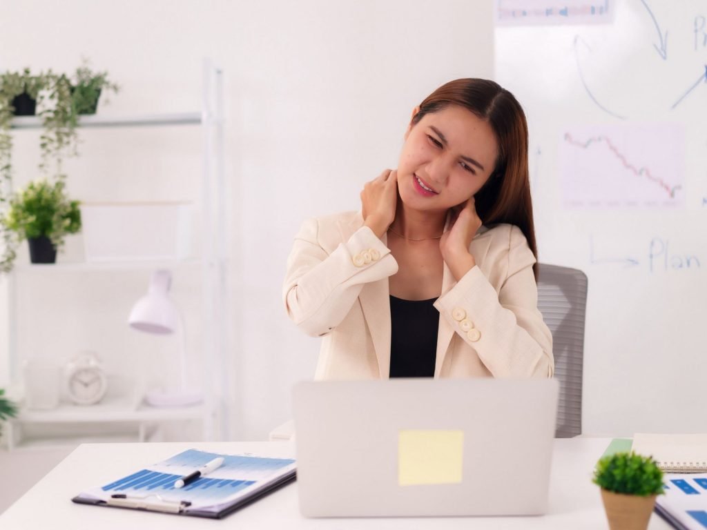 alt="A person sitting at a desk rubbing their neck in discomfort, illustrating the tension that causes cervicogenic headaches."
