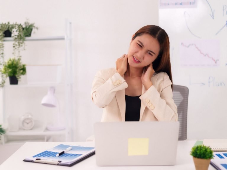 alt="A person sitting at a desk rubbing their neck in discomfort, illustrating the tension that causes cervicogenic headaches."