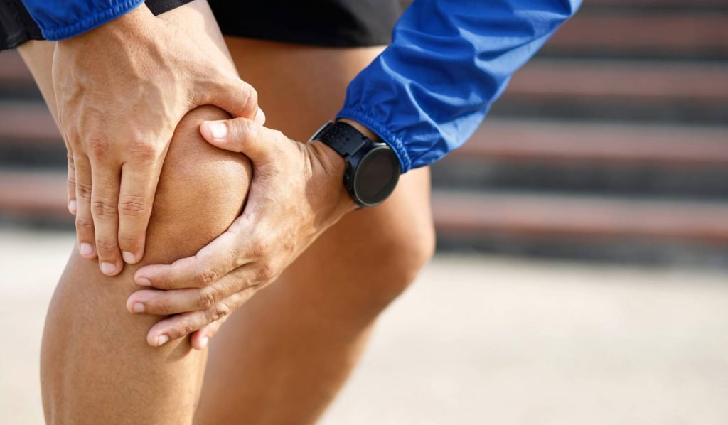 alt="A runner pausing to stretch their leg due to knee pain, highlighting how postural overload can impact performance and the need for a professional gait assessment."
