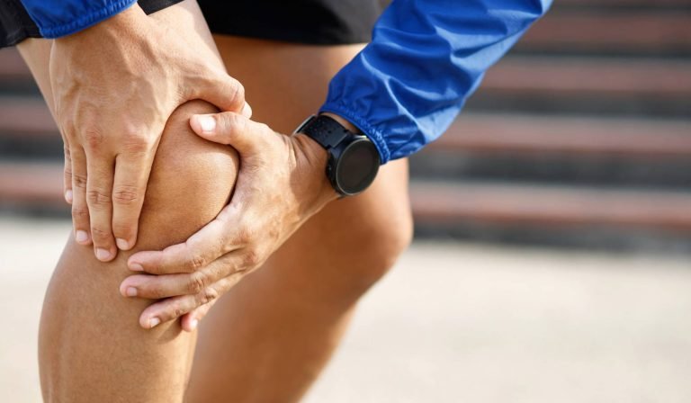 alt="A runner pausing to stretch their leg due to knee pain, highlighting how postural overload can impact performance and the need for a professional gait assessment."